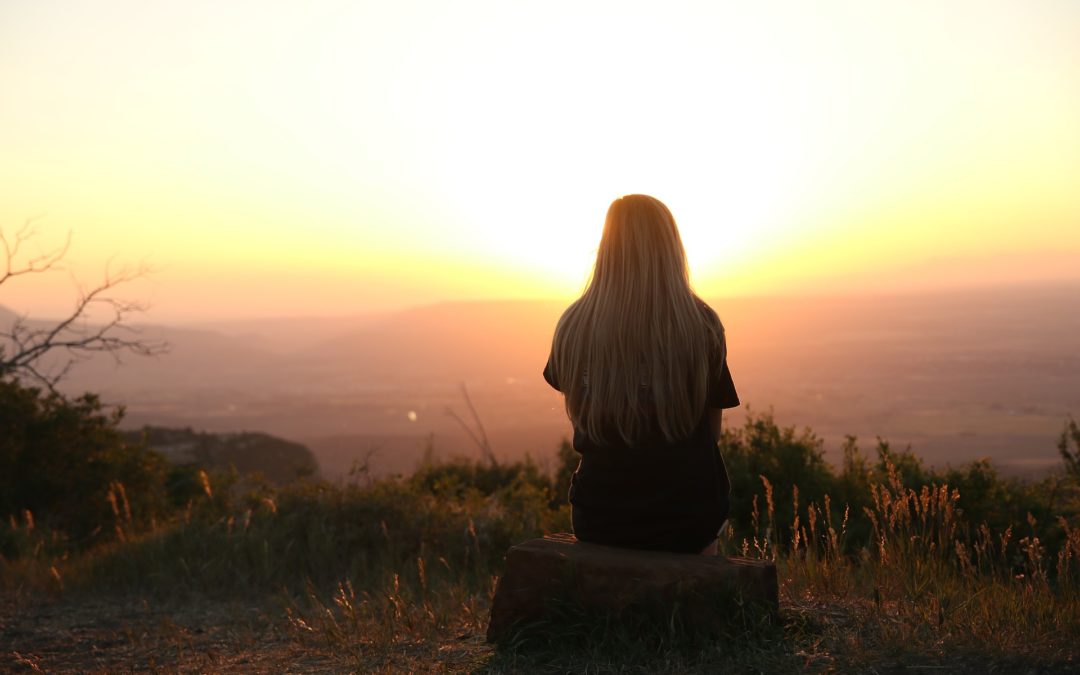 Woman sits alone watching a sunrise