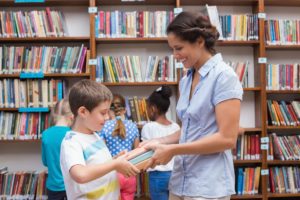 Elementary school librarian hands a book to students