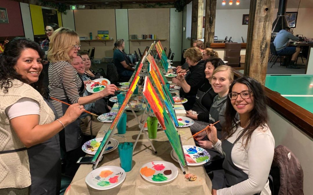 Staff smile at the camera while painting their own canvases at a Paint Night event.