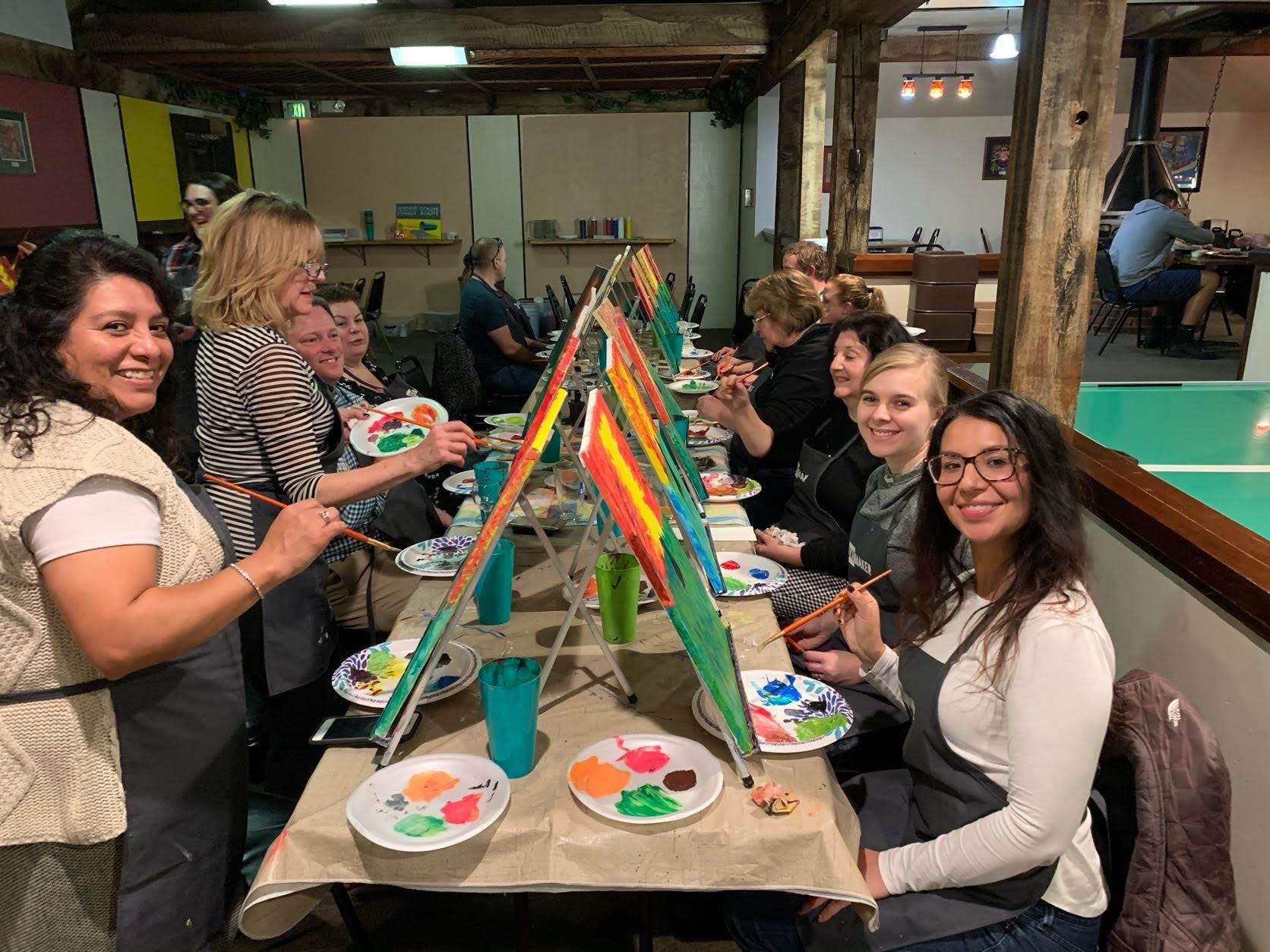 Staff smile at the camera while painting their own canvases at a Paint Night event.